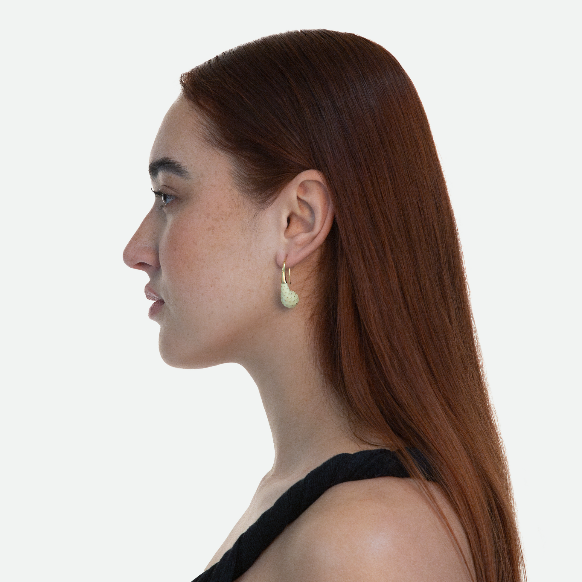Side profile of model wearing Aspera earrings evoking opuntia fruit with golden stem, designed by Ruggeri, on a white background.