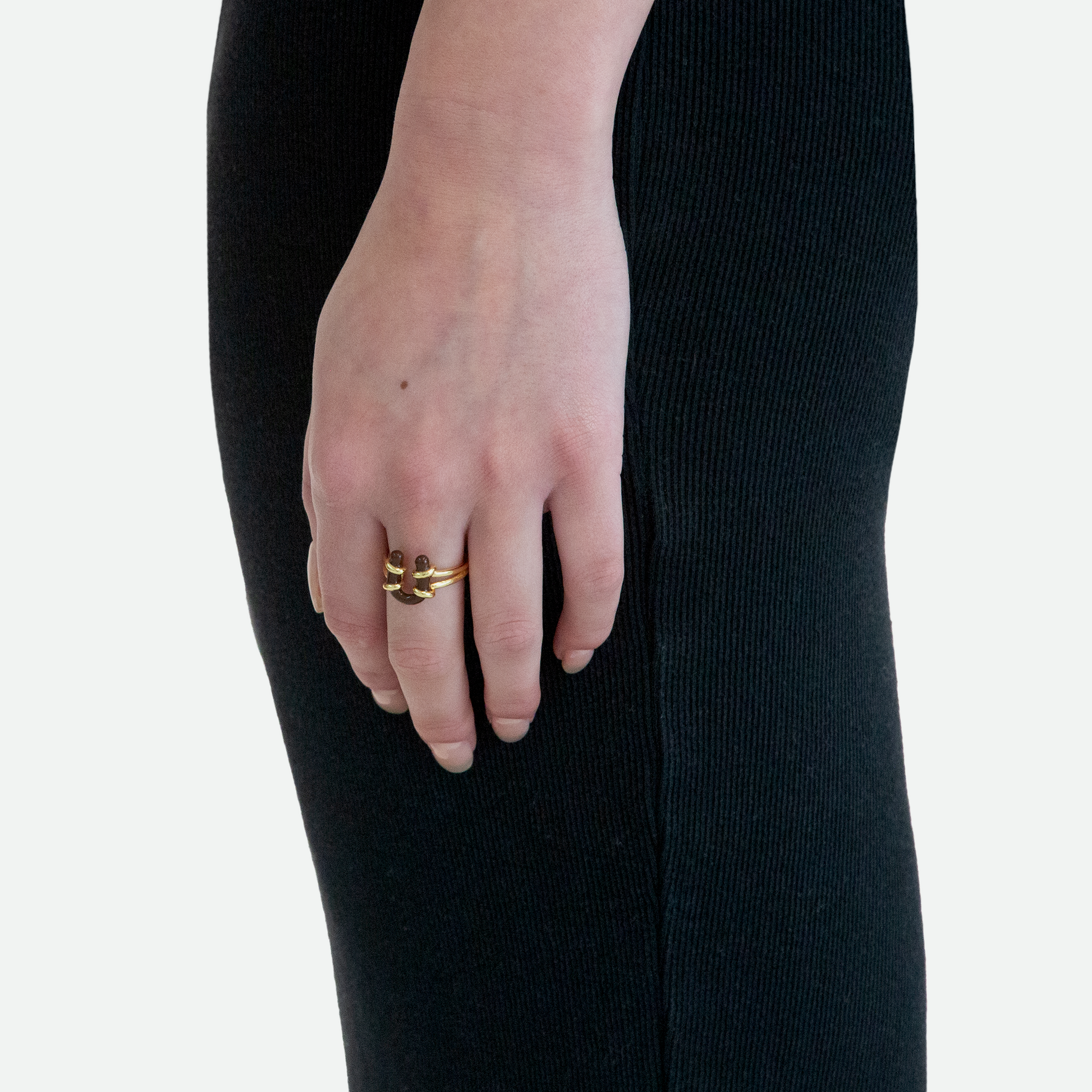 Side view of a model's hand wearing the Enamel Barbell Ring, emphasizing the coffee enamel U-shaped piercing within the contrasting golden loop, designed by Ruggeri.