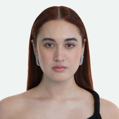 Model showcasing the Silver Lucci earrings, a silver plated statement piece adorned with sapphire cubic zirconia crystals, on a white background.