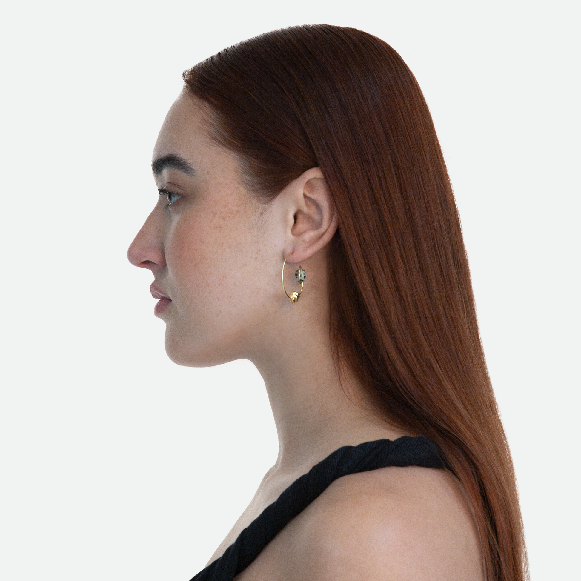 Side profile of model wearing the Orbit earrings that mirror a planet and its moon with a Dalmatian Jasper stone and bead set in a golden arc, on a white background.
