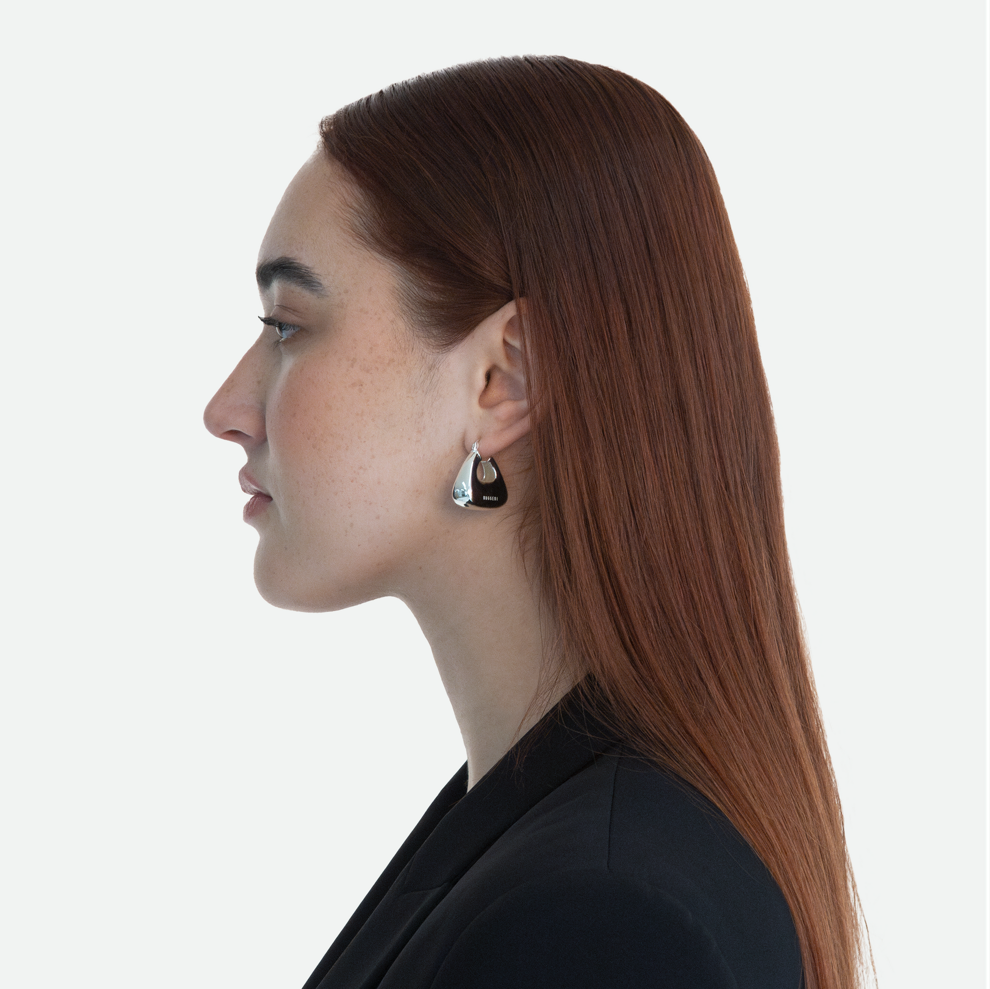 Side profile view of model wearing Ruggeri's silver Pouch earrings with etched logo.